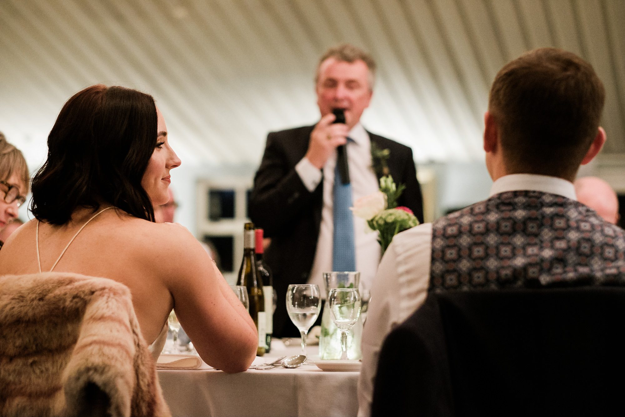 bride glancing across to groom during his father's speech