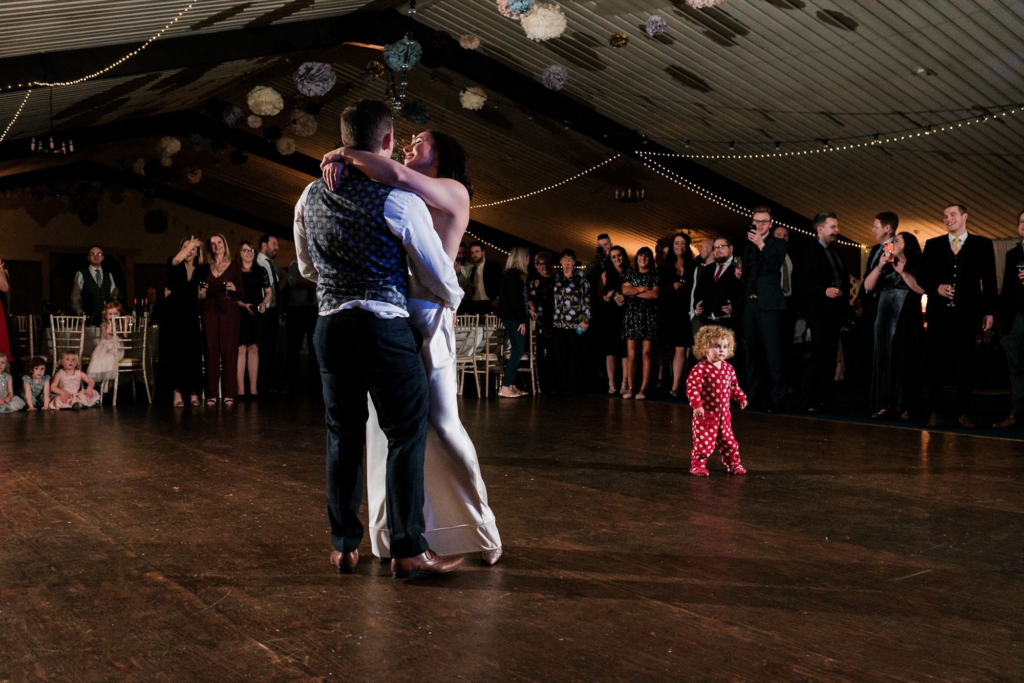 bride and groom's first dance with baby wandering across dance floor